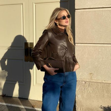 A woman posing outside in a chocolate brown leather jacket