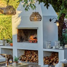 The White Company garden shot with large white wood burner, hanging rattan lgihts and table in shot