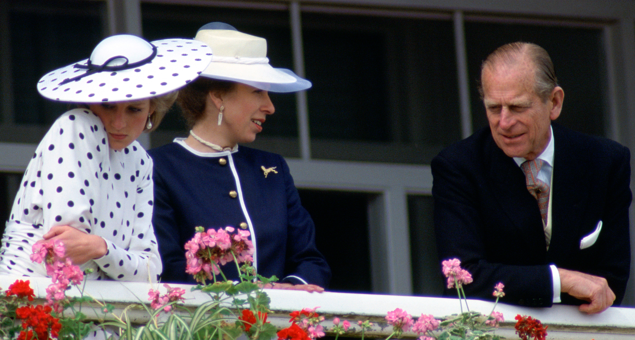Princess Diana wearing a white polka dot dress and hat looking sullen next to Prince Philip at the Epsom Derby
