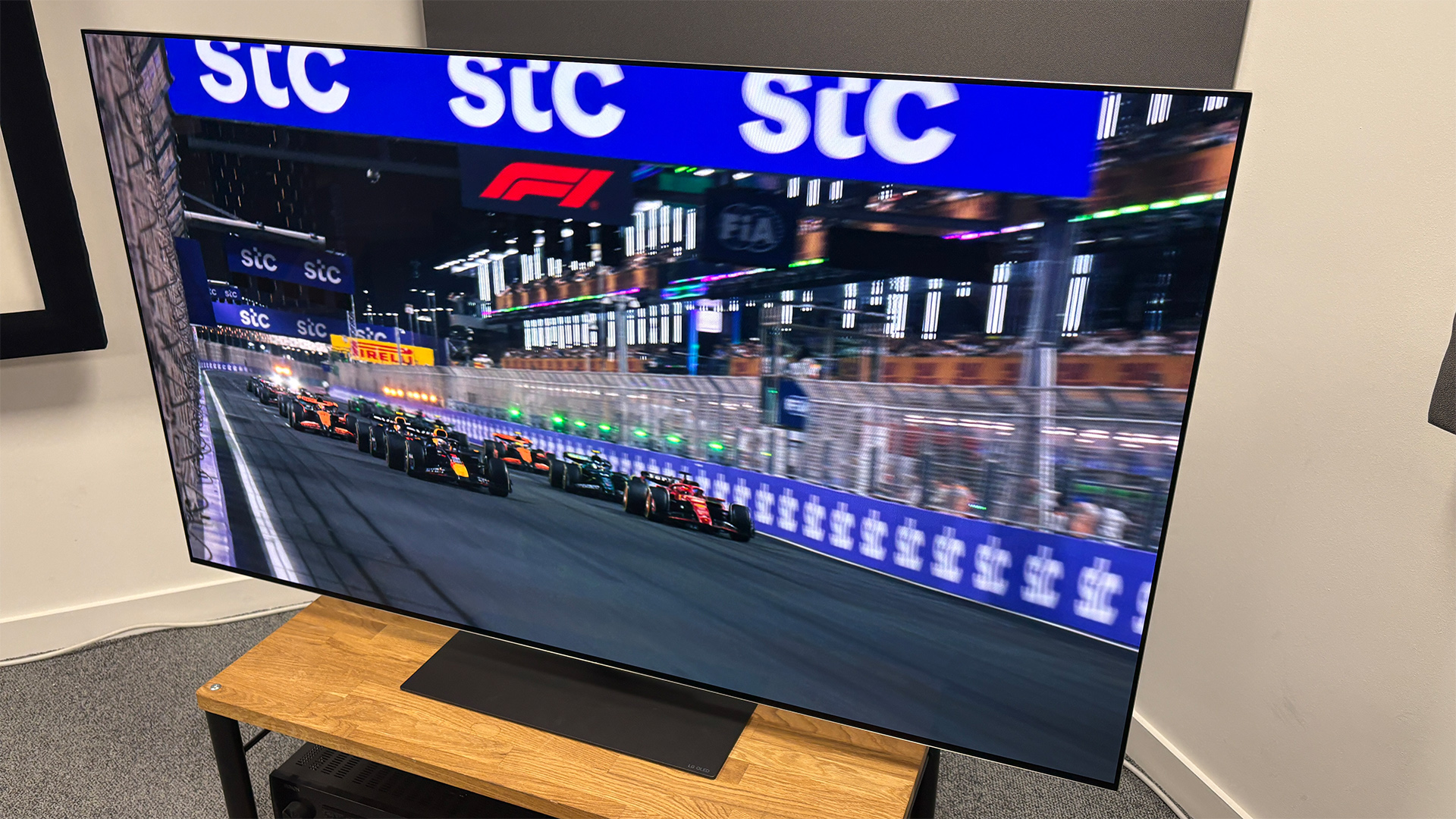 The 65-inch LG G5 OLED TV pictured on a wooden rack. On the screen is a still from Netflix F1 series Drive to Survive.