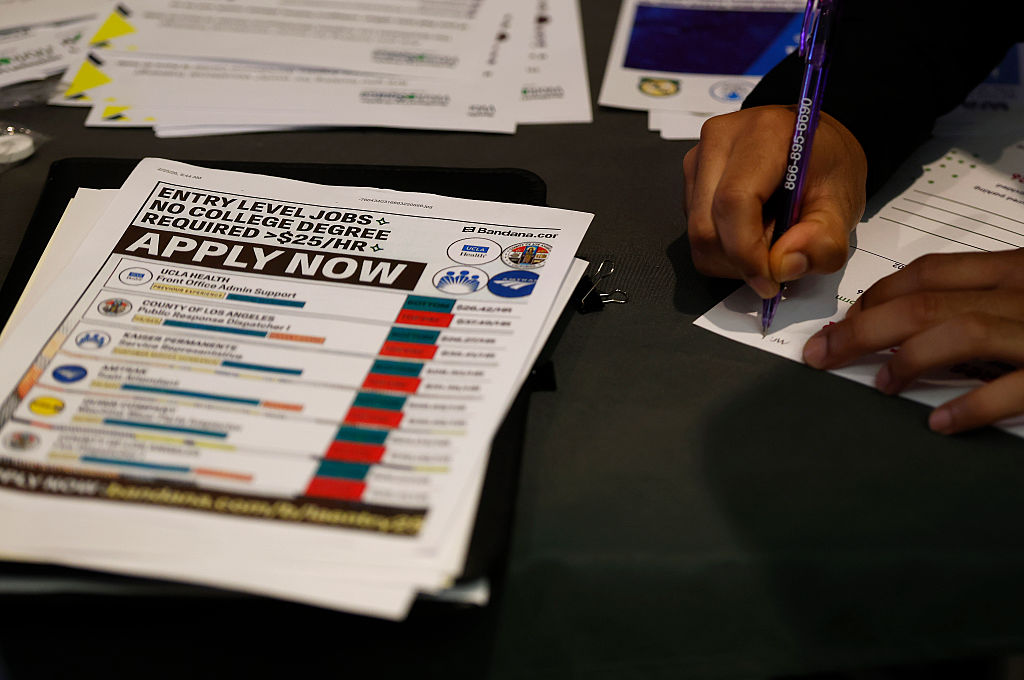 A person is filling out a job application at a job fair with an "Apply Now" flier next to them