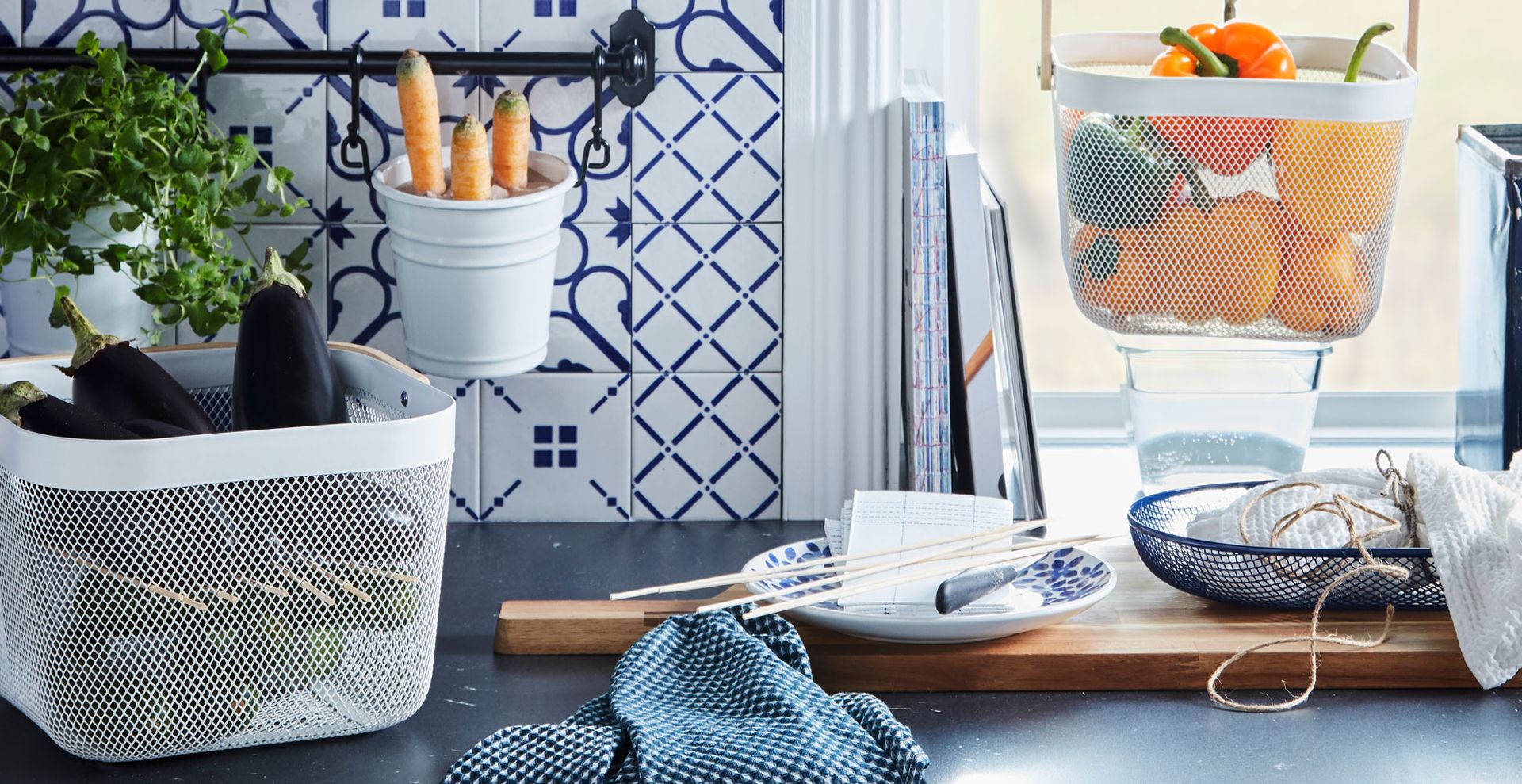 Wooden kitchen countertop with white metal storage basket filled with aubergines to demonstrate hoe effective baskets are for organizing kitchen countertops