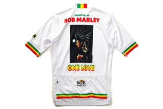 The back of a white State Bicycle Co Bob Marley edition jersey featuring red, yellow and green accents at the base and sleeves and featuring a One Love logo underneath a pic of Bob Marley in the center of the back of the jersey.
