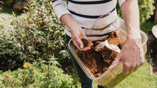 A woman with a bucket of coffee grounds ready to sprinkle them in the garden