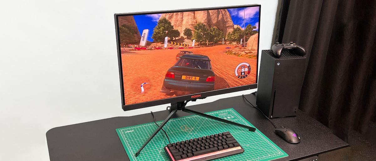 An AOC Agon Pro AG274QZM on a black desk with a green deskmat underneath