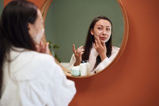 A woman looking in a mirror while applying skin products