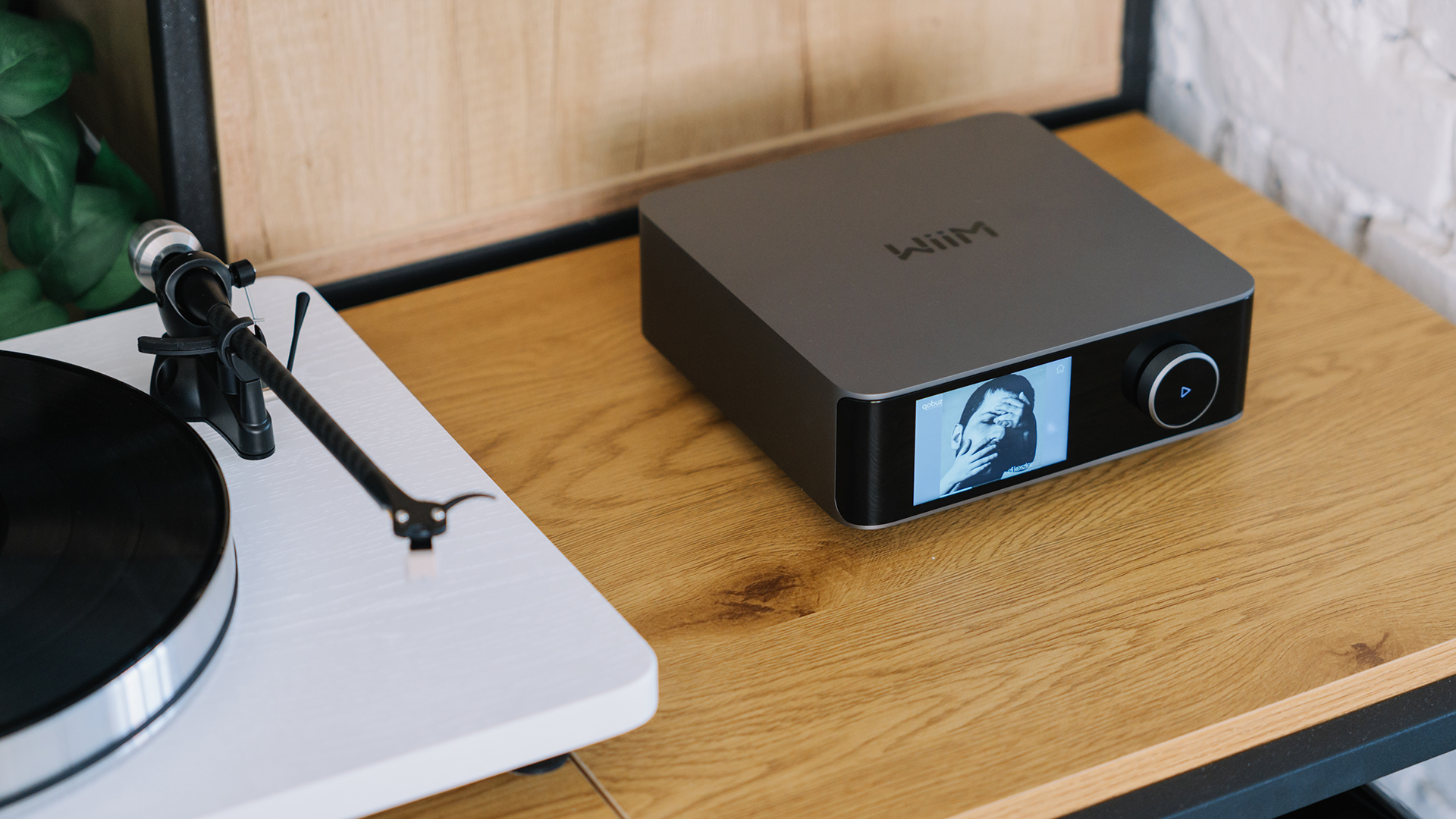 WiiM Amp Ultra on a wooden surface, next to a turntable