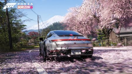 Forza Horizon 6 gameplay shows a silver Porsche driving through cherry blossom petals, and mount Fuji can be seen on the horizon