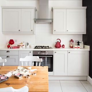 A white kitchen with a wooden dining table and red kitchen appliances