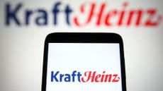 The Kraft Heinz logo on a smartphone, with the logo on a wall in the background too