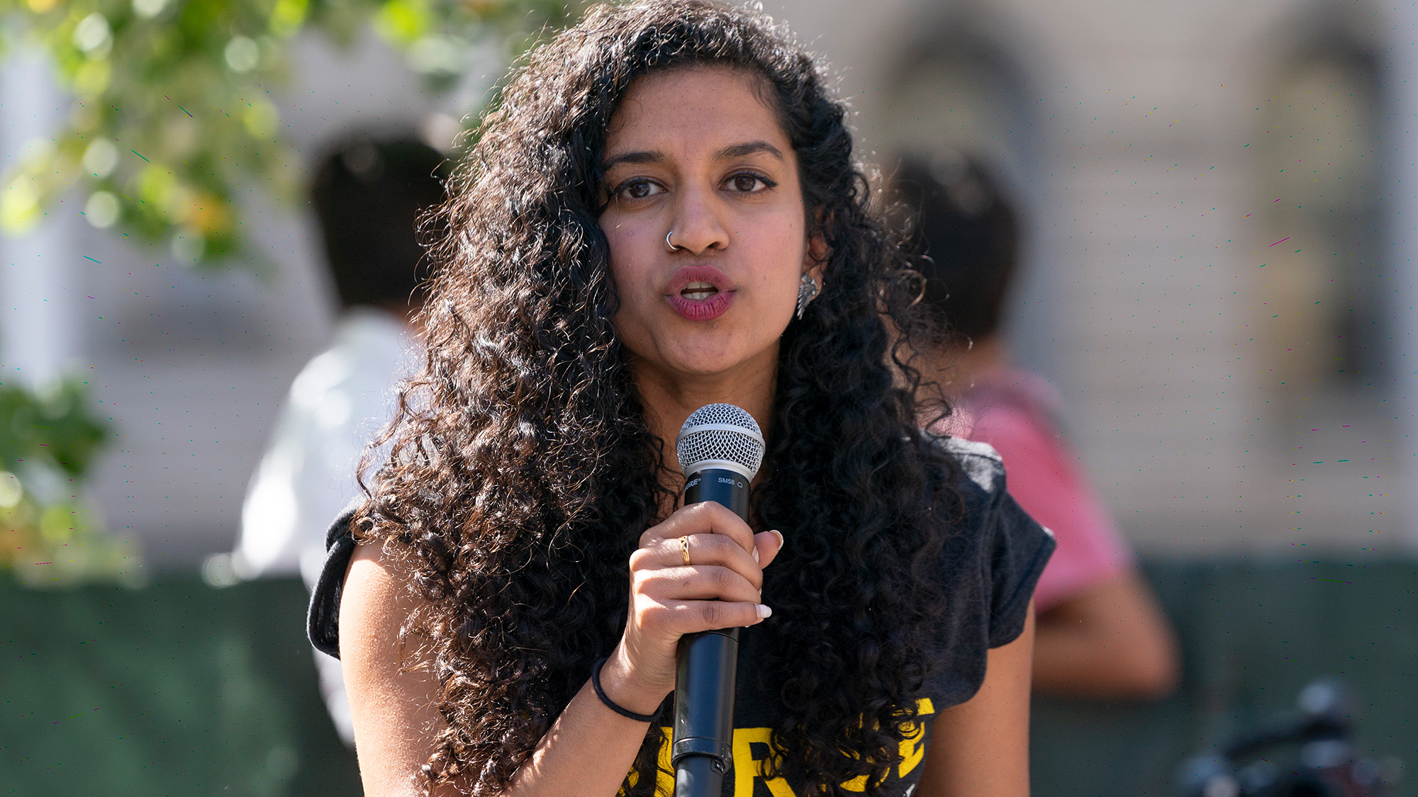 A woman with black curly hair speaks into a microphone at a climate rally