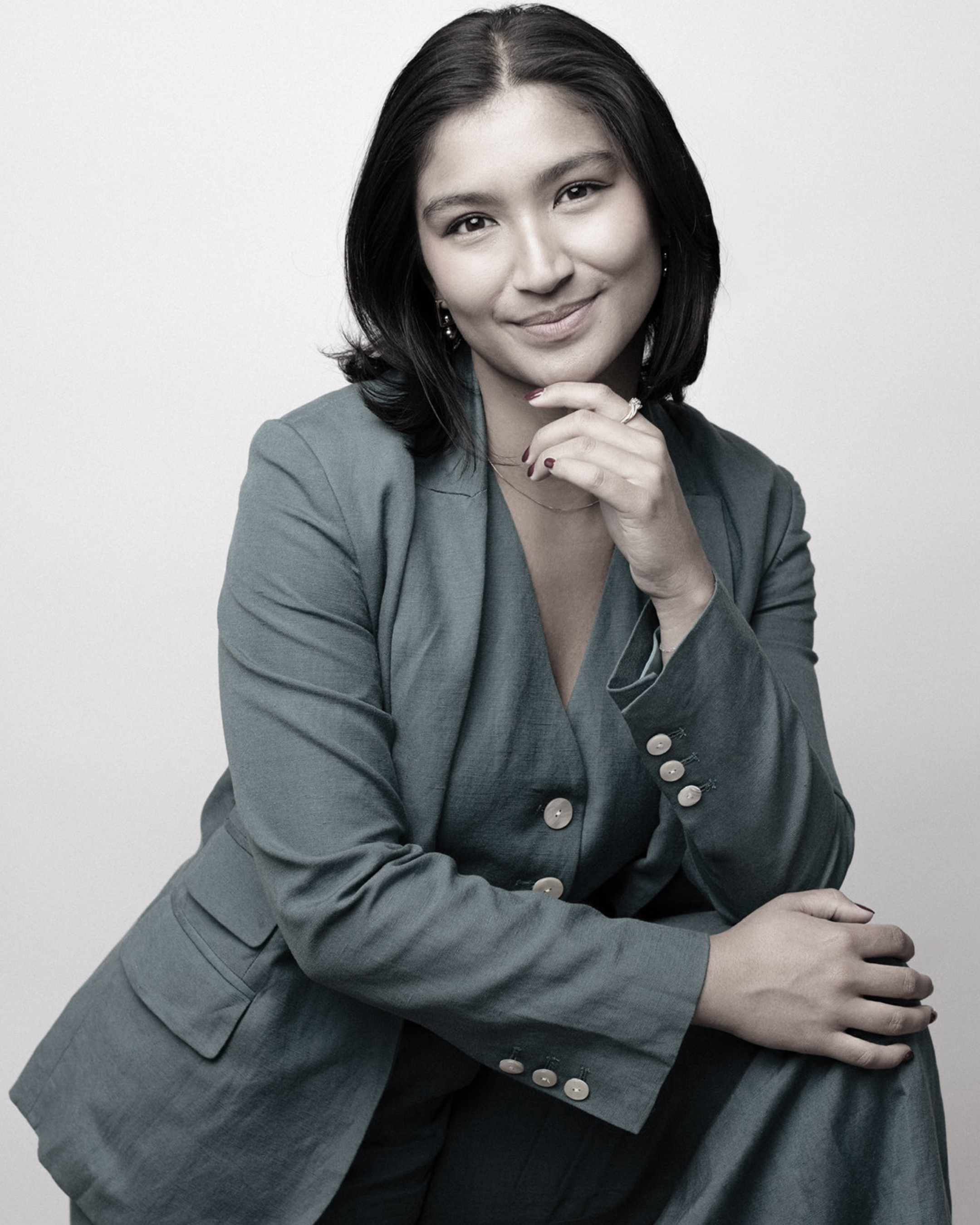 Deja Foxx seated in a suit with her hand resting on her chin.