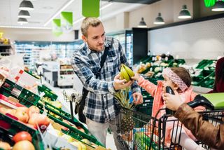 Dad handing bananas to his infant daughter who is sitting in a shopping trolley in a supermarket