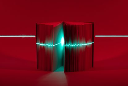 Laser beam scanning book in front of dark red background