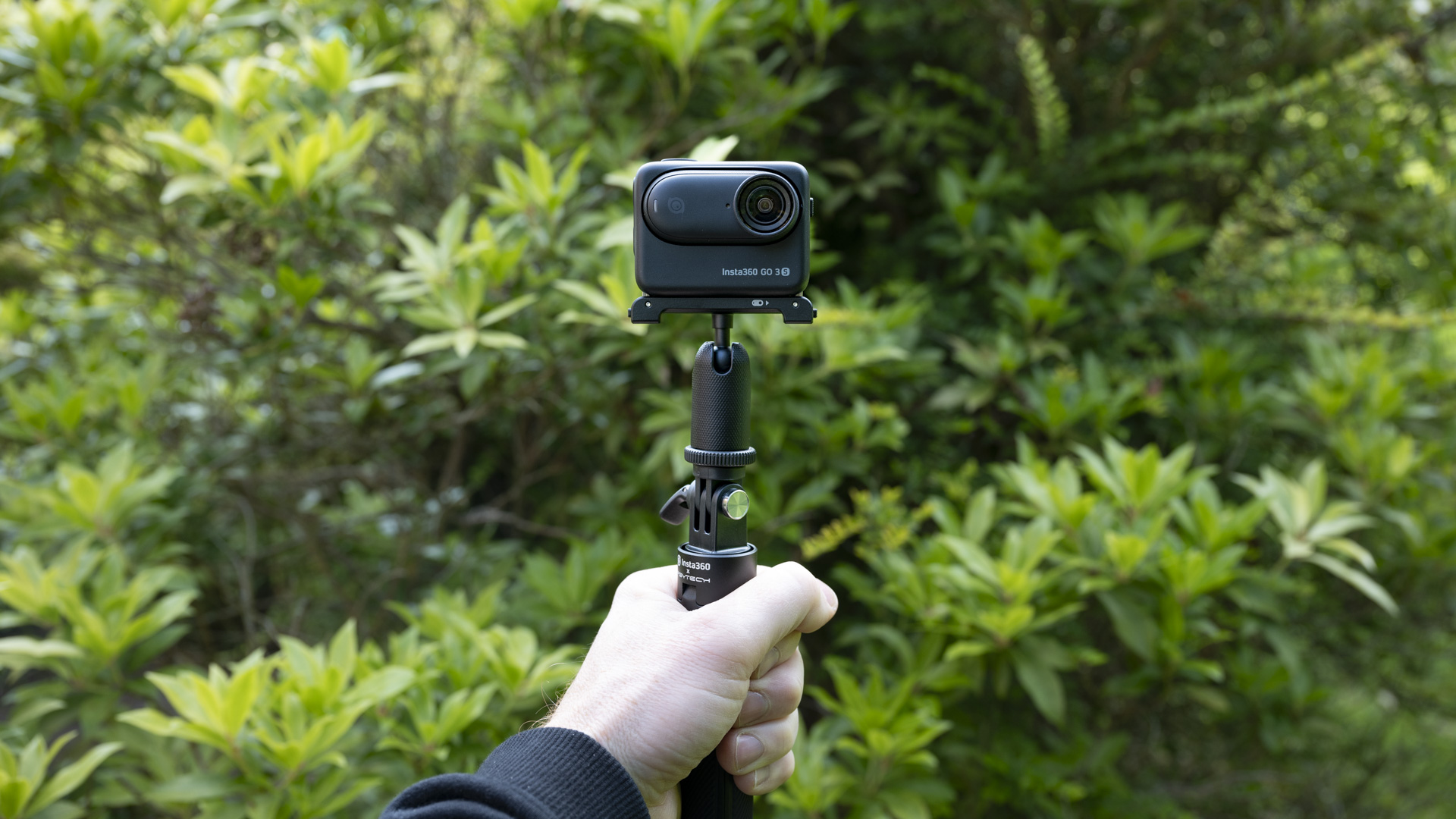 Insta360 Go 3S camera in its housing attached to a selfie stick, outdoors