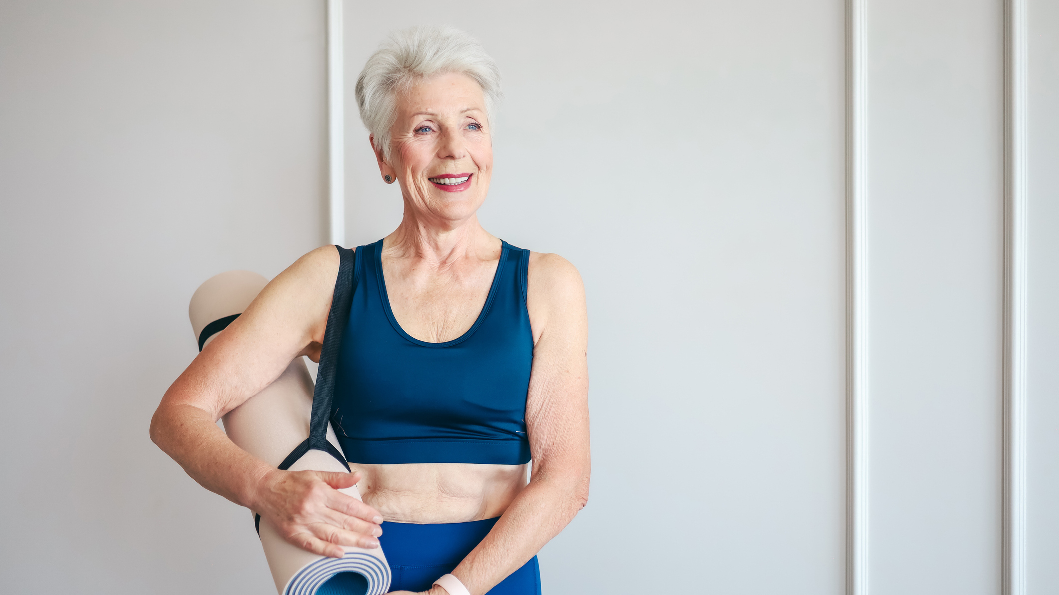 Woman with a rolled up mat secured with a strap slung over her right shoulder