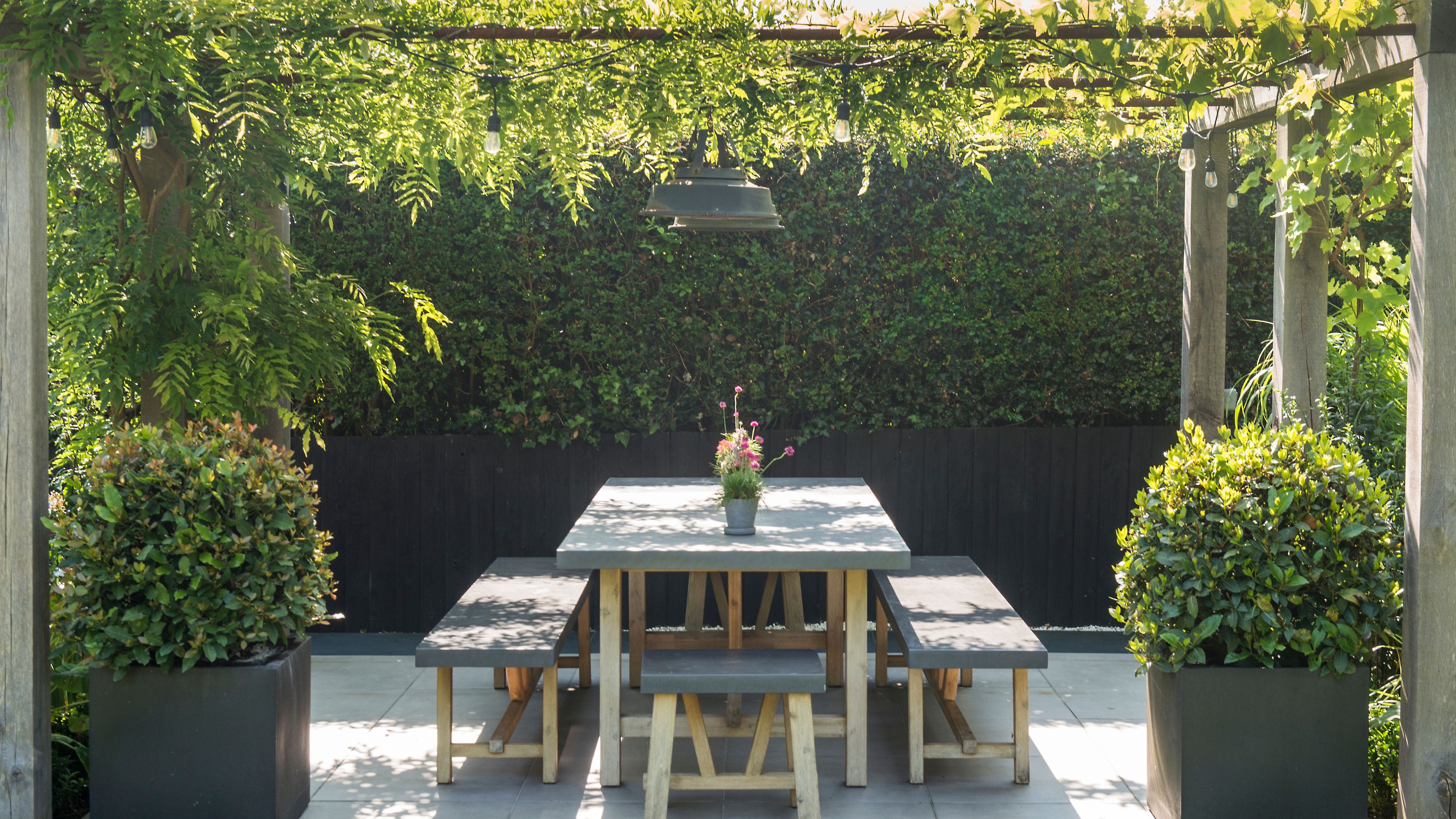 Outdoor dining area beneath pergola with string festoon lights and overhead pendant light