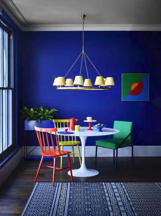 blue dining room with brightly coloured table and chairs, large pendant light with yellow shades