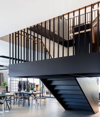 Interior view of Dunhill's HQ featuring tables, chairs, stools, a showroom with rails of clothing, green plants in pots and a black staircase