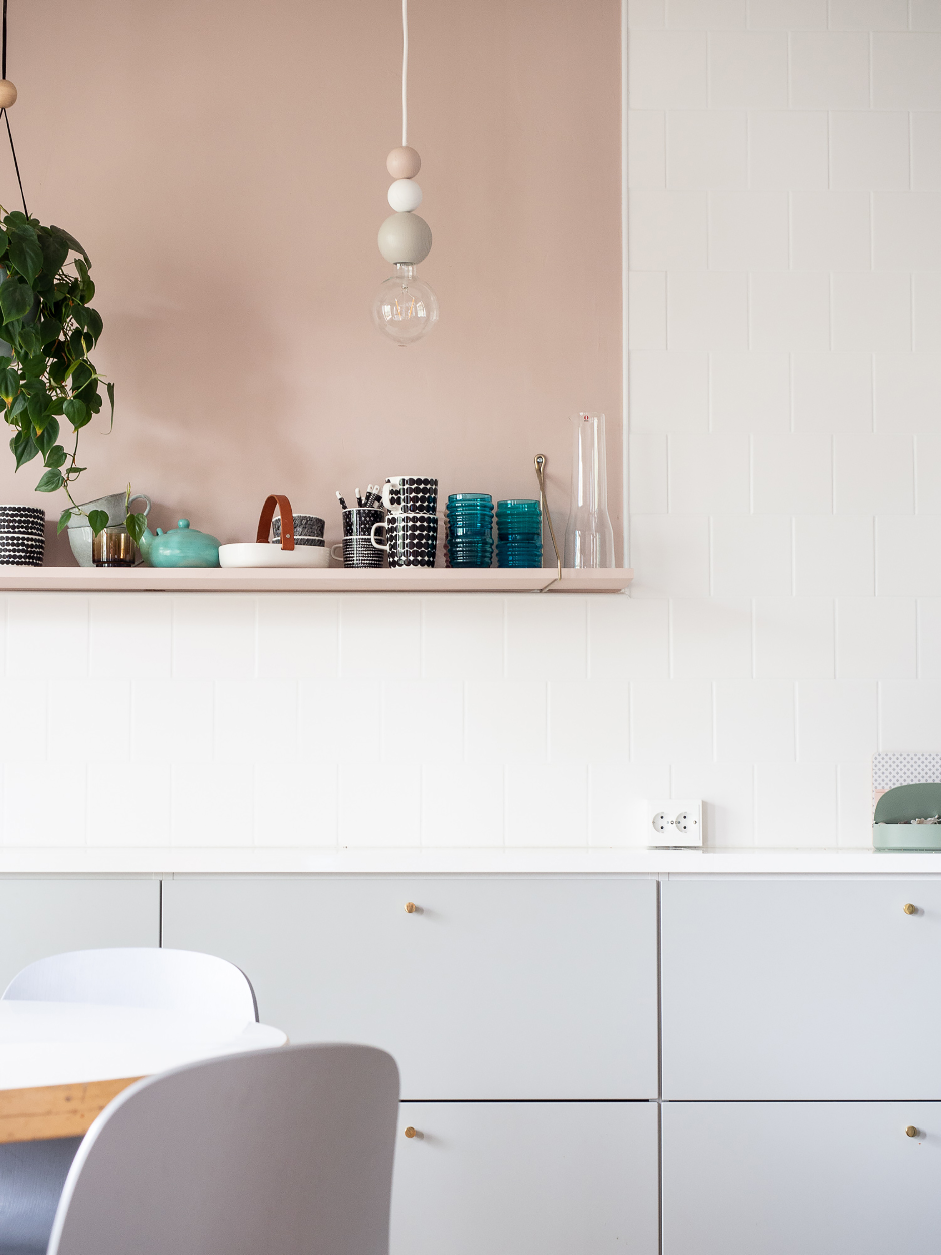 A kitchen with white walls, grey cabinetry and pink recess styled with various ceramic and plants by QUU Design