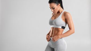 Woman standing against grey backdrop in activewear looking down at her stomach