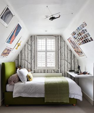A teenage boys bedroom idea in a loft space with grey and white forest wallpaper, model airplanes and posters on the walls