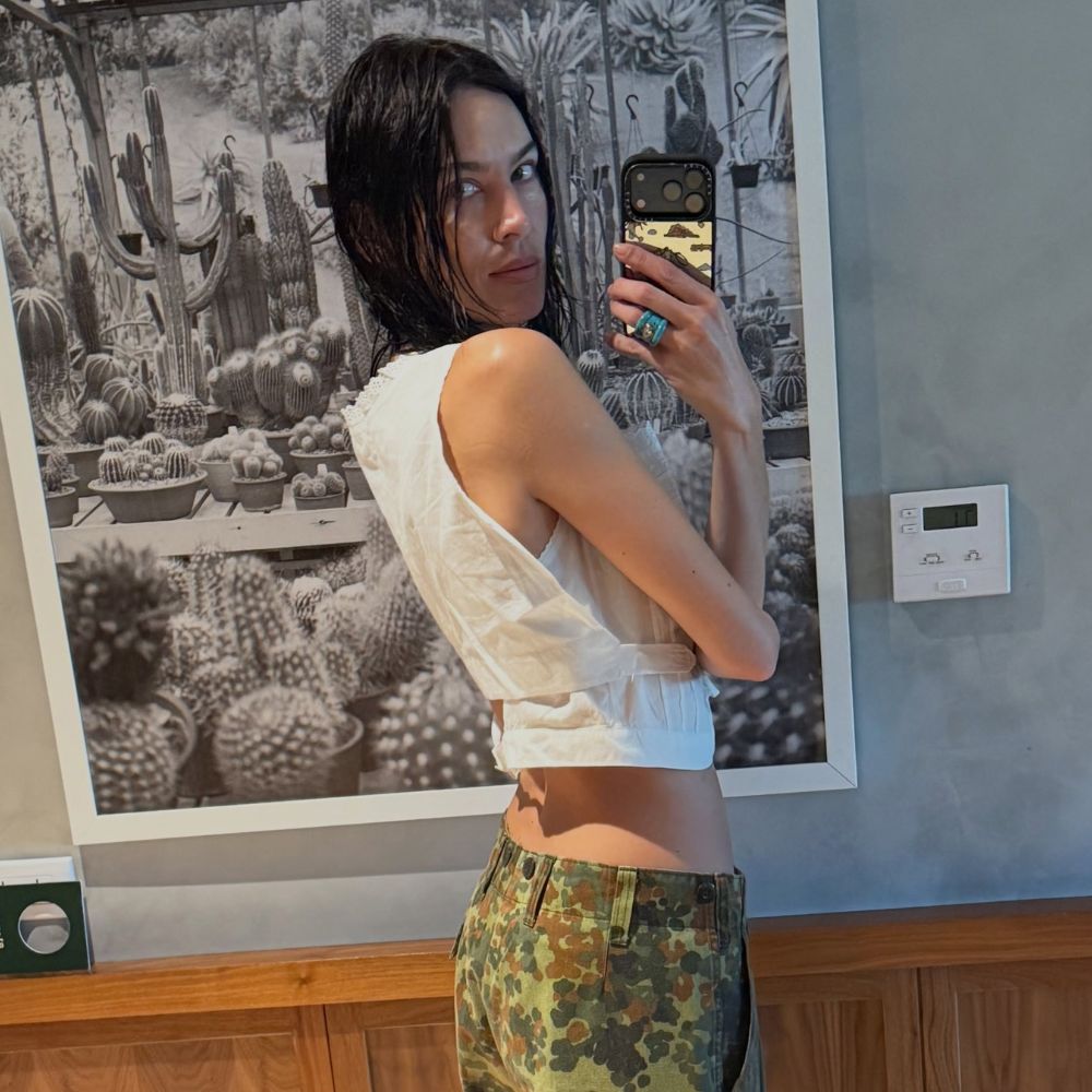 Alexa Chung takes a mirror selfie wearing camo trousers with a white cropped top.