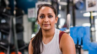 Poorna Bell, part of the How Exercise Changed My Life series on woman&home, sitting on a bench in the gym looking at the camera wearing workout clothes