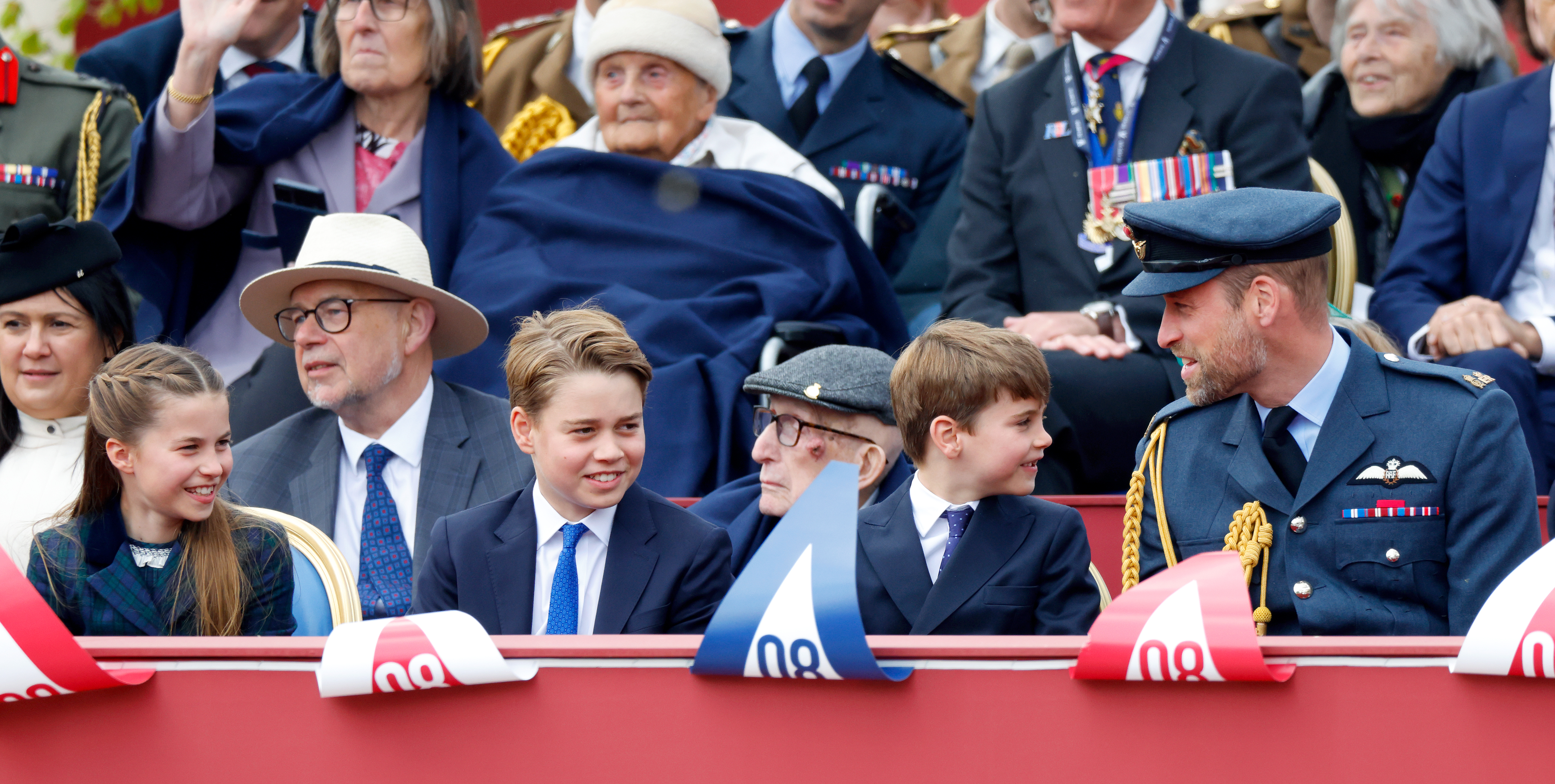 Princess Charlotte, Prince George, Prince Louis and Prince William sitting in a row at a VE Day parade