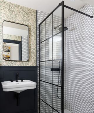 A small bathroom with botanical wallpaper and a black-framed glass shower screen