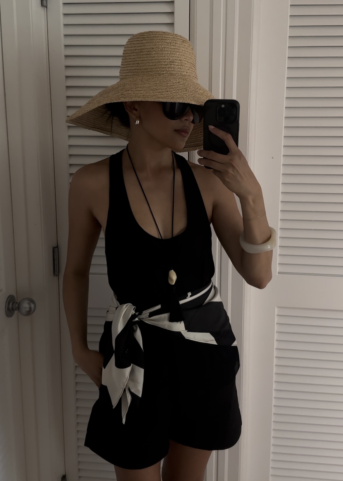 Dawn Tan wearing a black tank top, shorts, black and white scarf as a belt, and straw hat