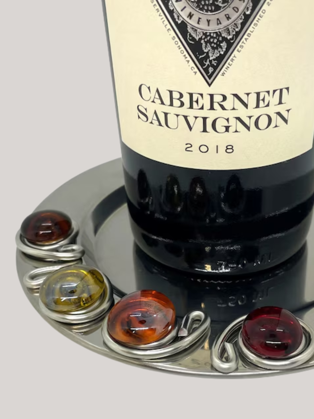 A close-up of a wine bottle on a steel coaster with a beaded border from Swiddlesinc on Etsy