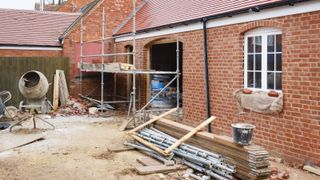 A building site with a red brick home being worked on with scaffolding and a cement mixer in the background