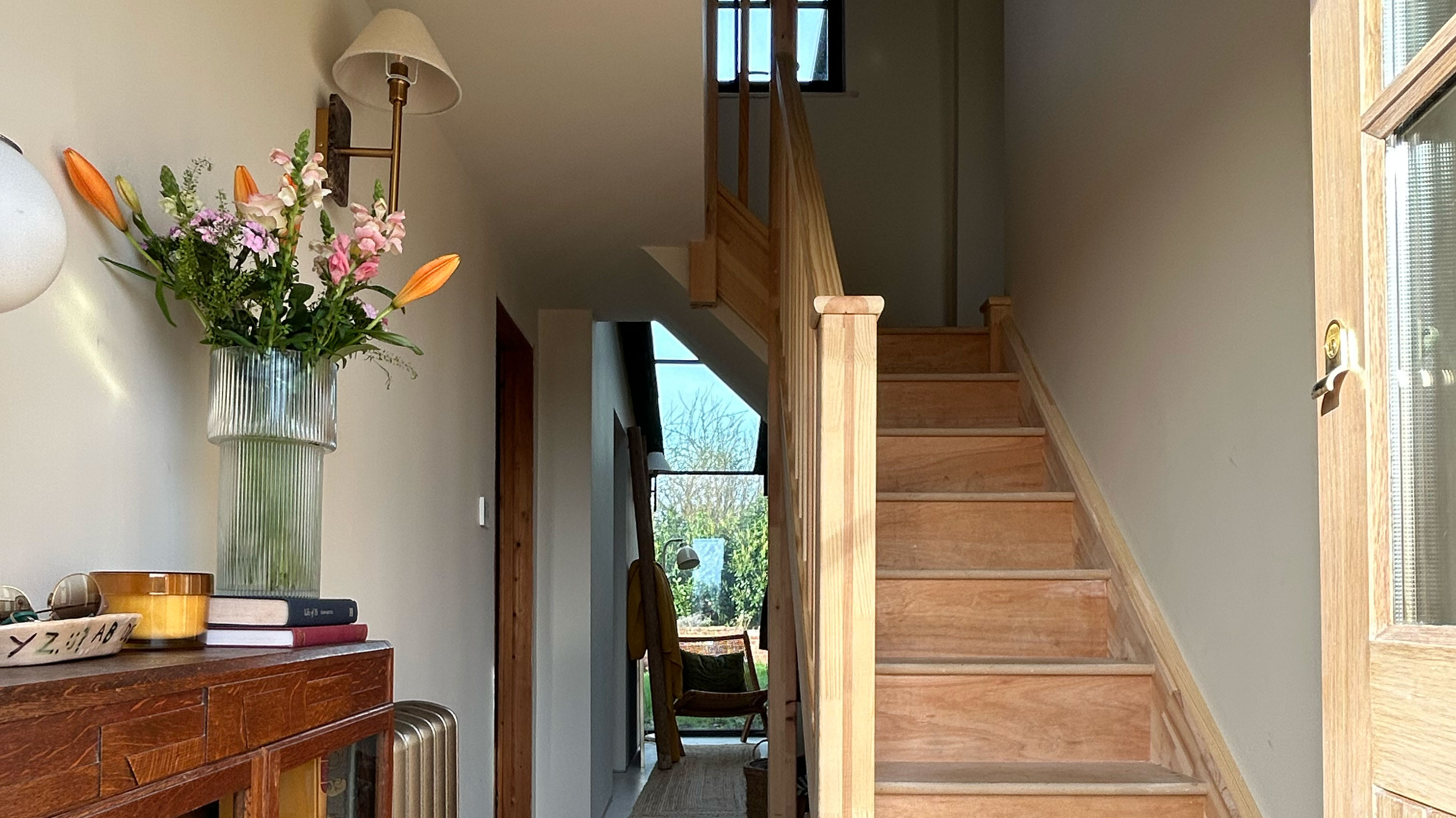 Hallway with wooden sideboard decorated with candle and vase of flowers beside unfinished staircase