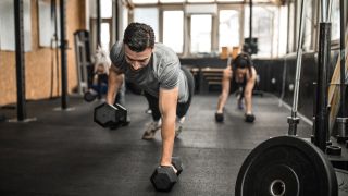 People in gym perform renegade row back exercise with dumbbells