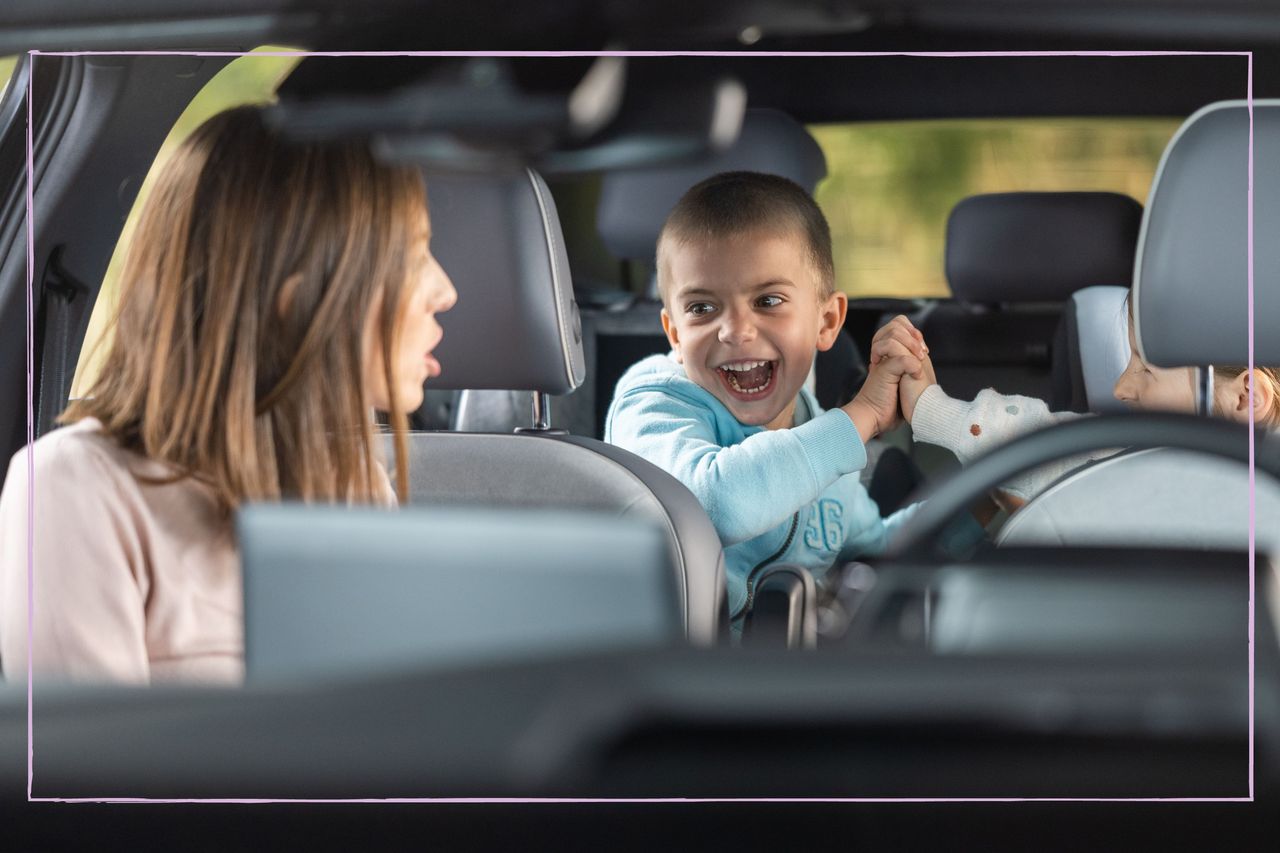 A young boy in the back of a car grinning while being told off