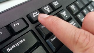 Outstretched finger pointing to the print screen button on a keyboard
