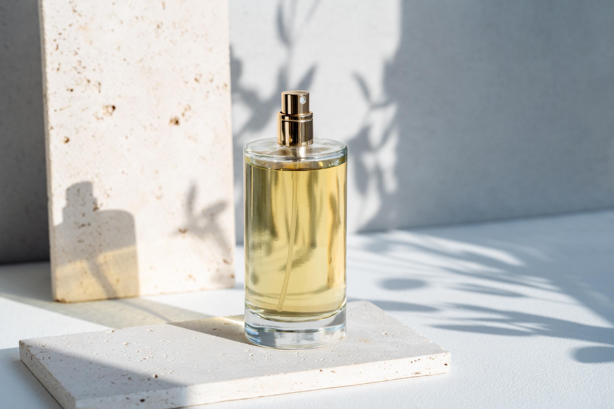  A glass perfume bottle displayed on a white table draped in a soft glow of natural sunlight. 