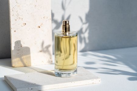 A glass perfume bottle displayed on a white table draped in a soft glow of natural sunlight.