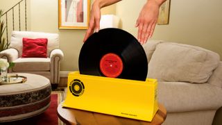 Eine Frauenhand hält eine Vinyl-Schallplatte in einem gelben Spin-Clean Schallplattenreinigungssystem.