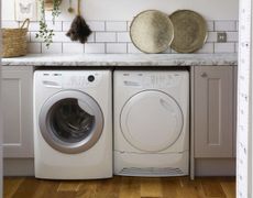 utility room with white washing machine and tumble dryer on wooden flooring against white wall tiles