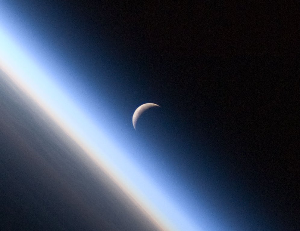 A setting, waning crescent moon amid the thin line of Earth&#039;s atmosphere.