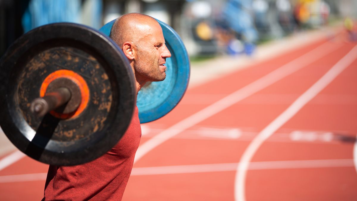 Man performing barbell squat on running track