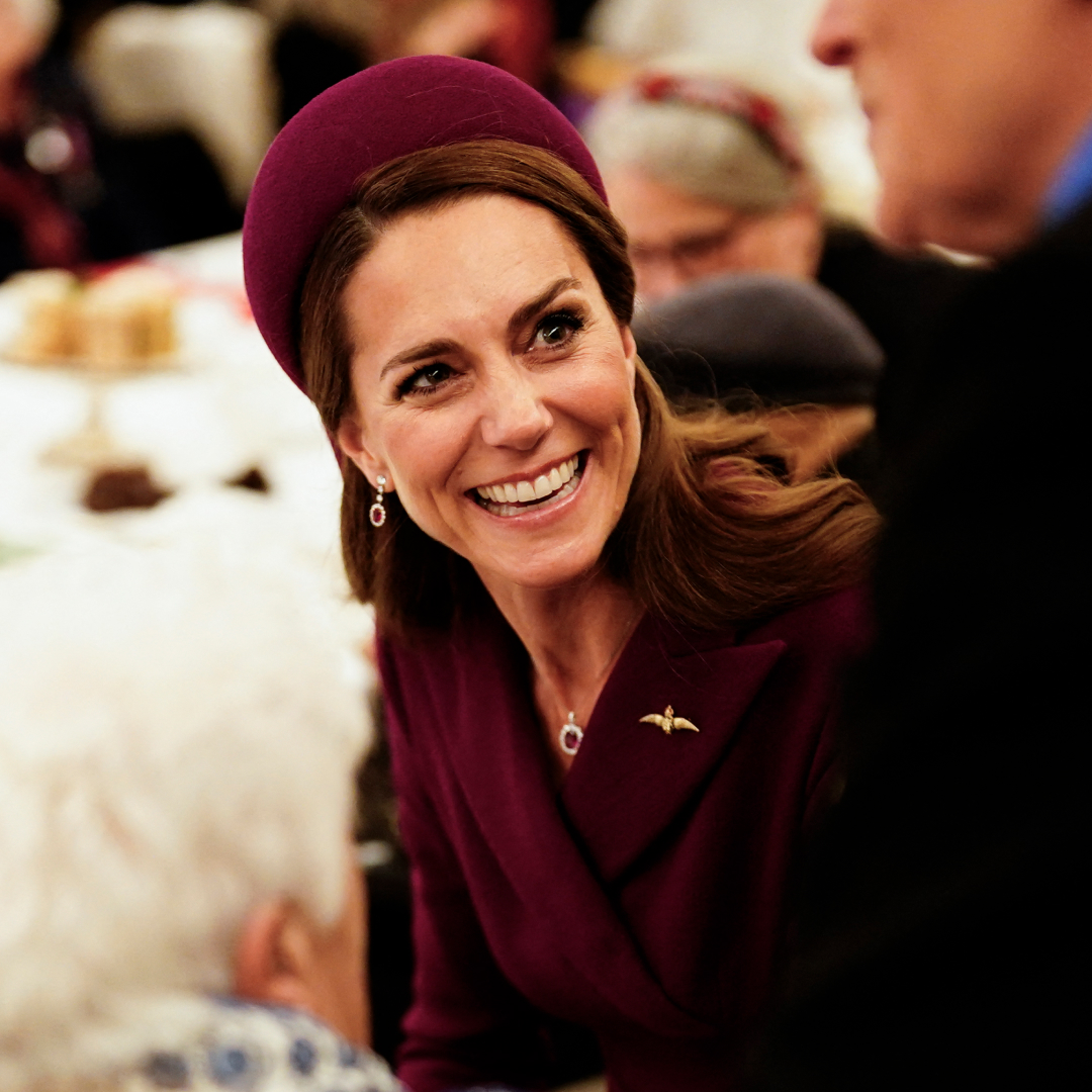 Kate Middleton wears a wine red coat dress and matching hat and laughs