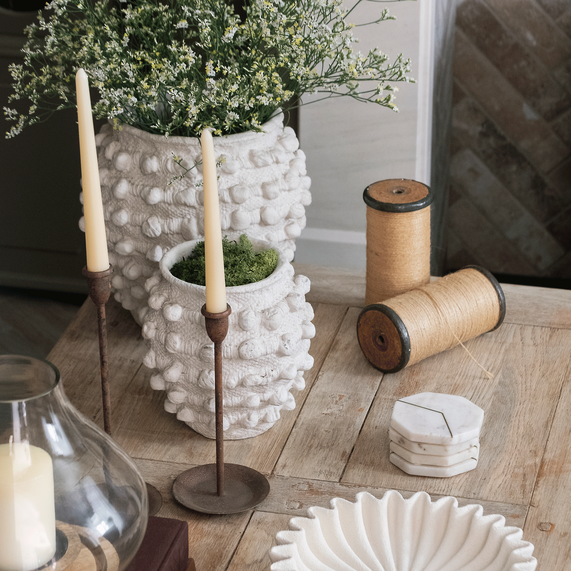 a close up of a neutral coffee table with plant pits candles and a carved bowl