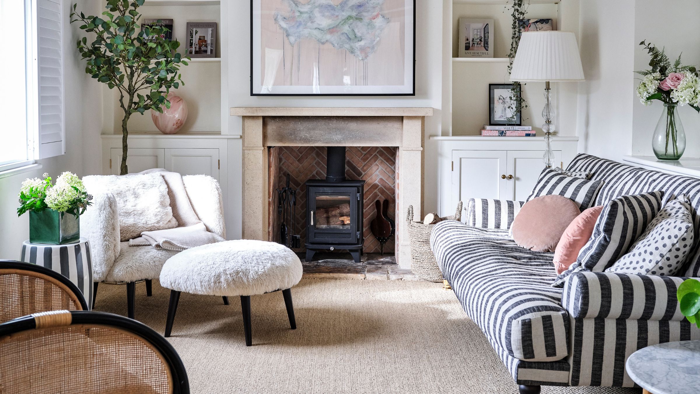 Cottage-style living room with a log burner on the back wall, a black and white striped sofa on the right and a white fluffy accent chair on the left