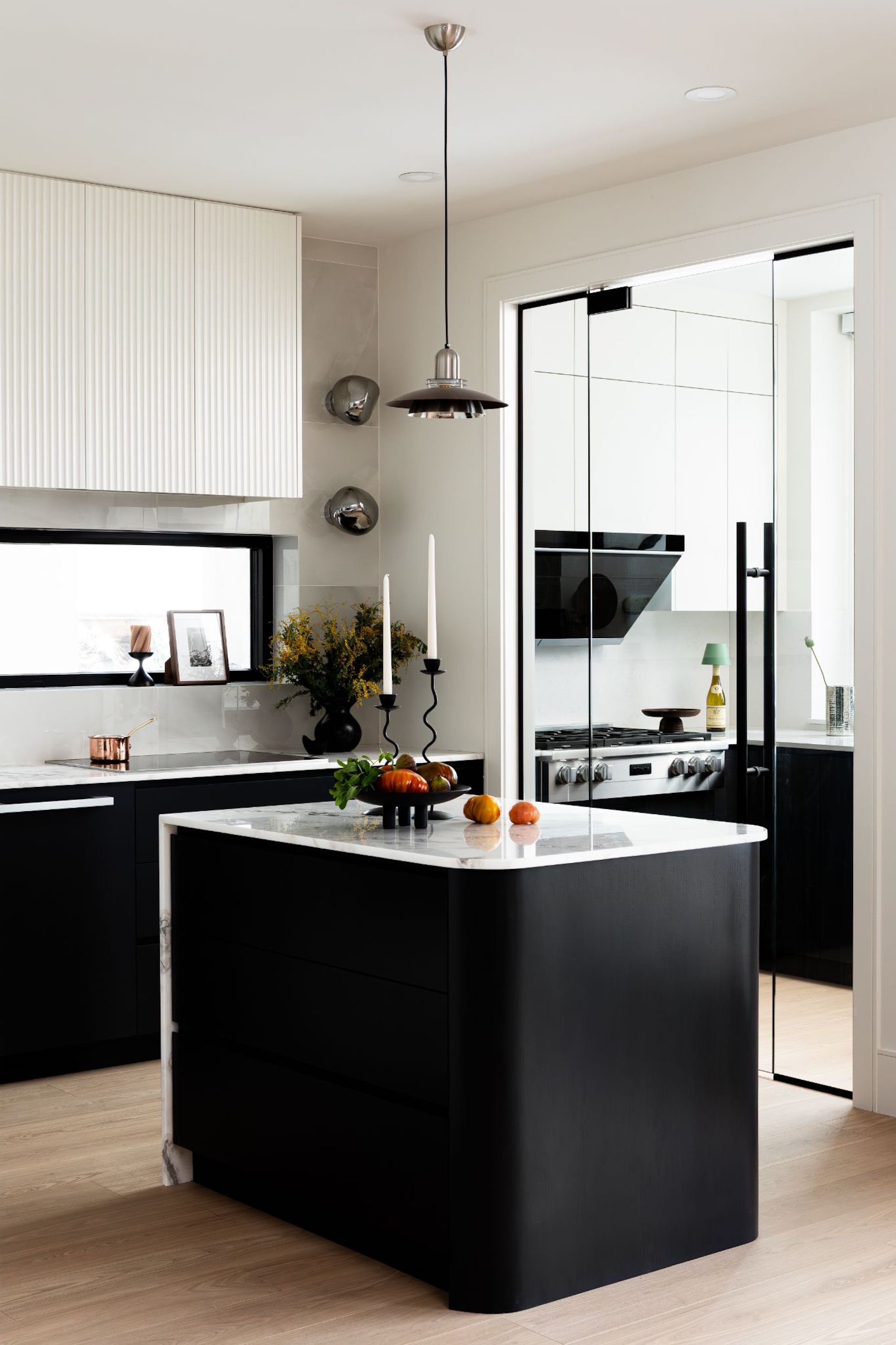 A view of the kitchen through the glass door into the second kitchen area with a gas cooker and all white cabinetry.