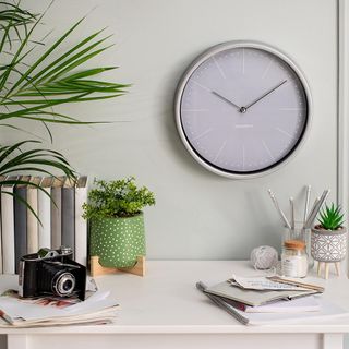 Hallway table with camera, books and pot plant next to grey wall with round clock