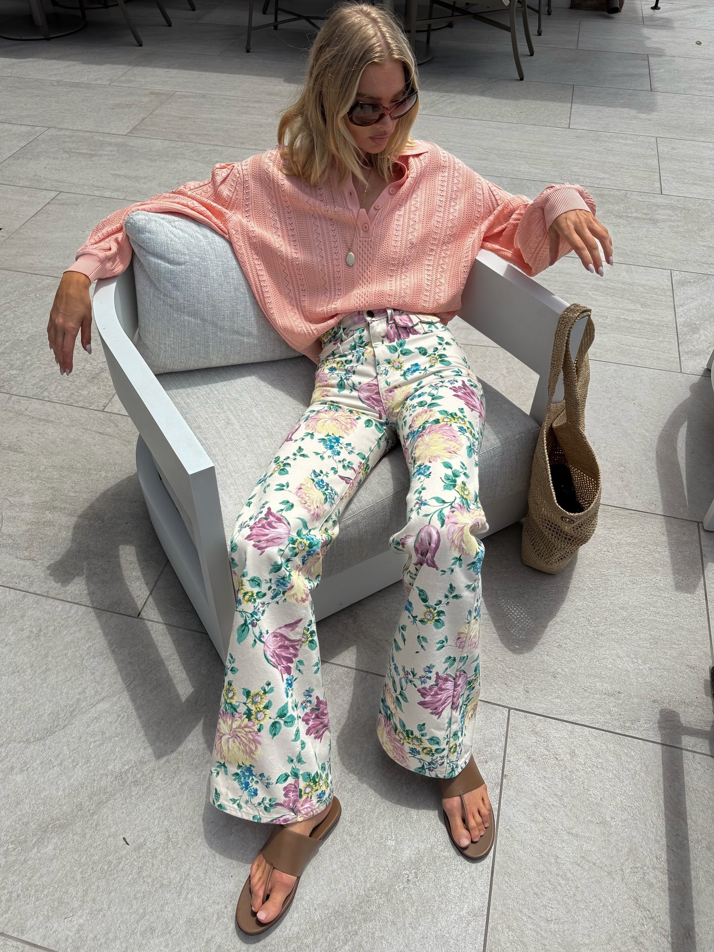 Model @hoskelsa sits on an armchair wearing floral high-waisted jeans with suede sandals and a peach lightweight knit.