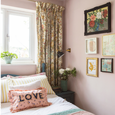 a pink painted bedroom with colourful bedding and patterned bedroom curtains over window